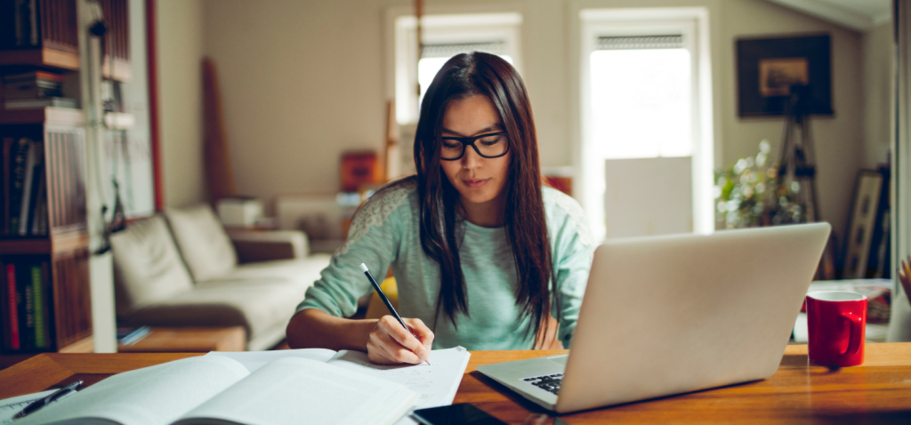 Woman writing at desk with open laptop